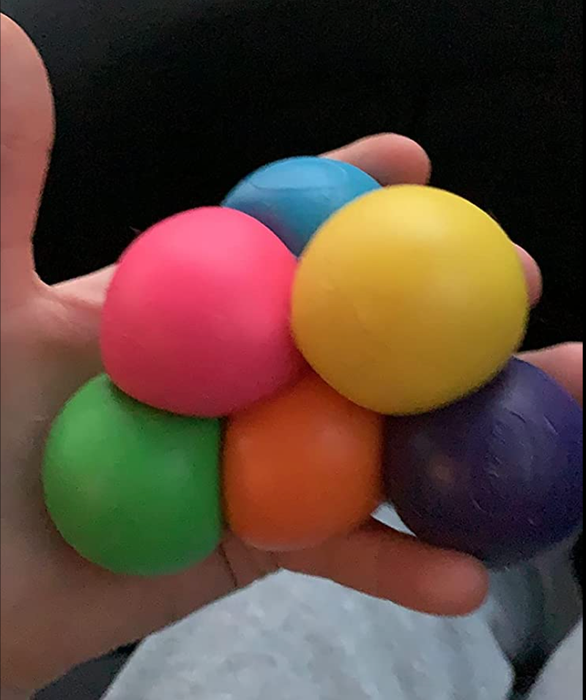 A reviewer holding six colorful, squishy balls in various shades of the rainbow in their hand.