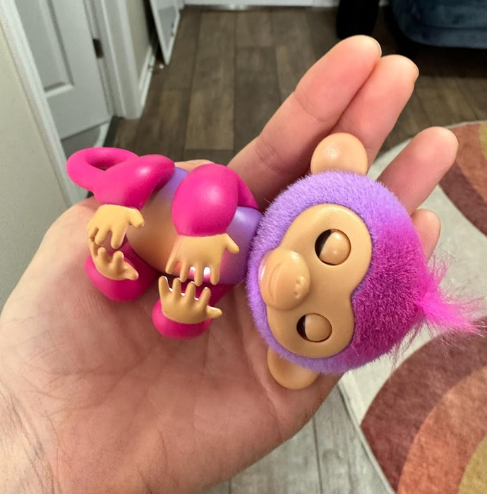 A hand holding a small toy monkey with a fuzzy purple and pink body