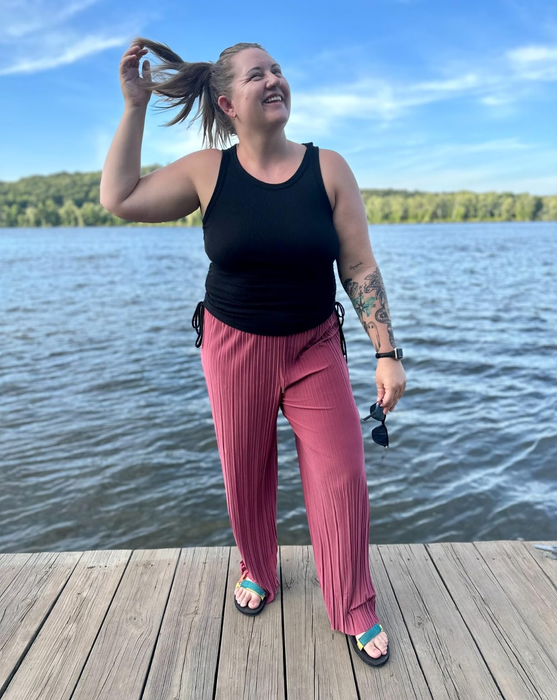 Another reviewer wearing the mauve pants on a dock with a scenic water backdrop