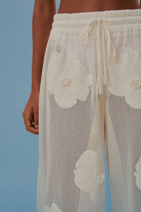 A detailed close-up of lace-trimmed drawstring pants set against a vibrant blue background.