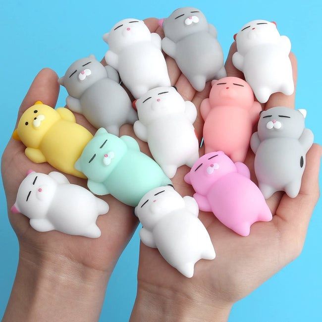 Hands holding a set of 12 squishy toys shaped like sleeping cats.