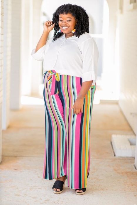 A model styled in wide-leg pants featuring vibrant multi-colored vertical stripes and a tie waistband.