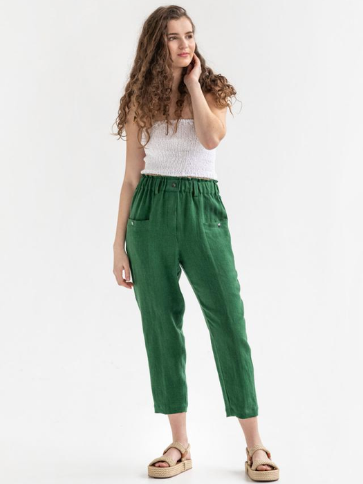 A model is wearing green pants with a white tank top and tan sandals.