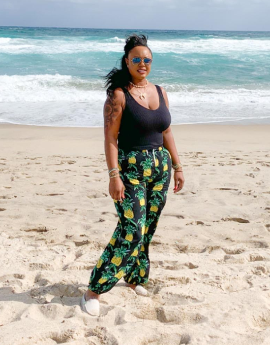 a reviewer pictured wearing the pineapple-print pants on a sunny beach
