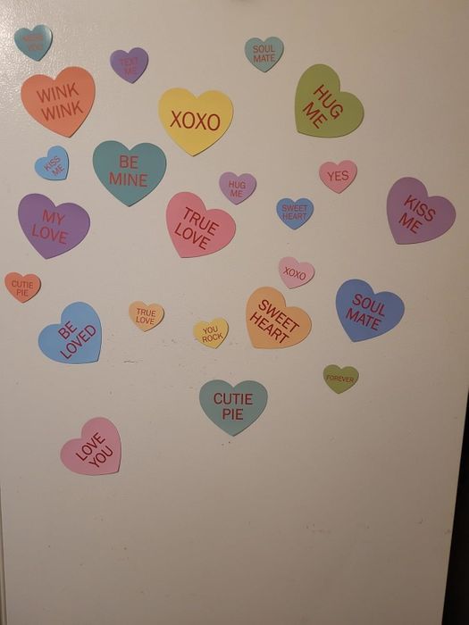 A set of colorful heart-shaped magnets featuring phrases like 'Be Mine,' 'Wink Wink,' 'XOXO,' 'Hug Me,' and 'Sweetheart' displayed on a white background.