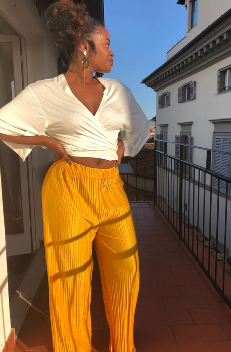 A reviewer posing on a balcony in stylish yellow pleated palazzo pants