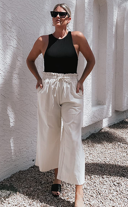A reviewer is wearing white pants paired with a black tank top and sandals.