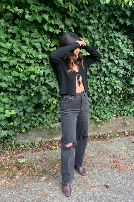 A reviewer models the distressed black jeans in a casual pose