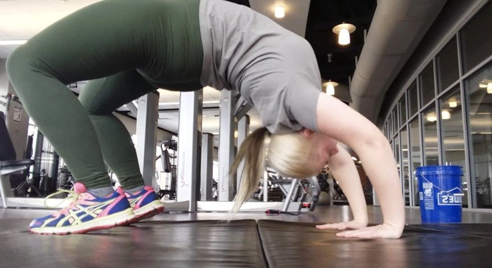 A reviewer performing a backbend in green leggings at the gym.