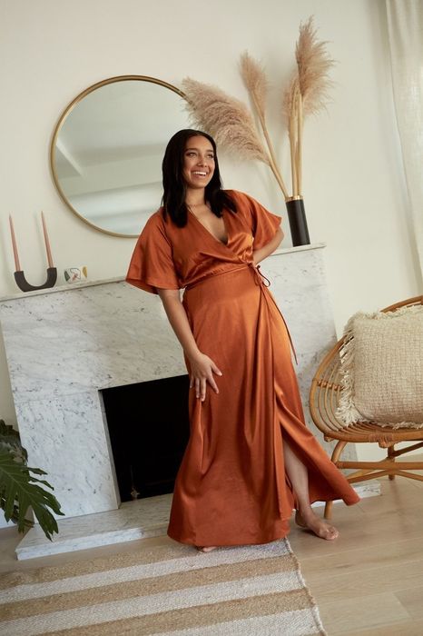 A model wearing the rust-colored dress by a fireplace.