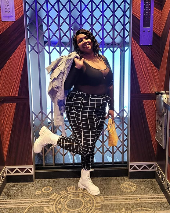 A reviewer showcasing the black pants adorned with a white grid design, paired elegantly with white boots.