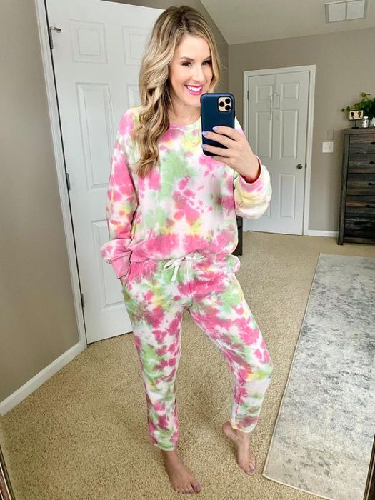 A woman dressed in a tie-dye sweatshirt and joggers, holding a phone, epitomizing laid-back, casual fashion.