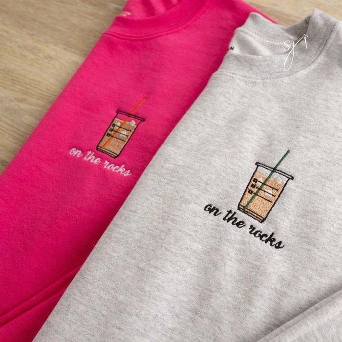 A pink sweatshirt and a gray sweatshirt, each with an iced coffee embroidered on them and