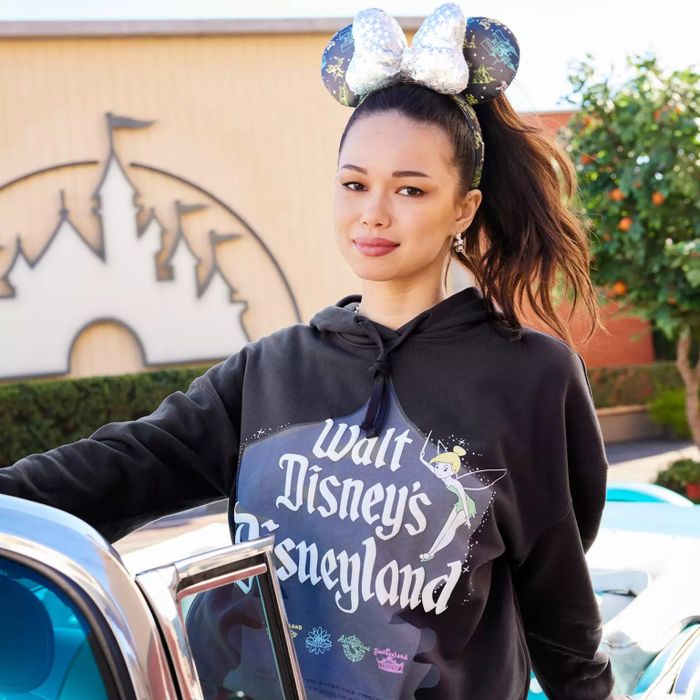 A model wearing a black hooded sweatshirt with Walt Disney's Disneyland logo and Tinkerbell design.