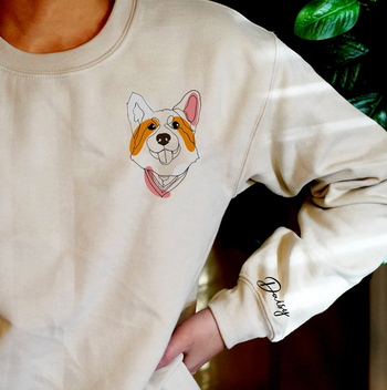 A model sporting a white sweatshirt featuring a corgi graphic near the shoulder, complete with its name.
