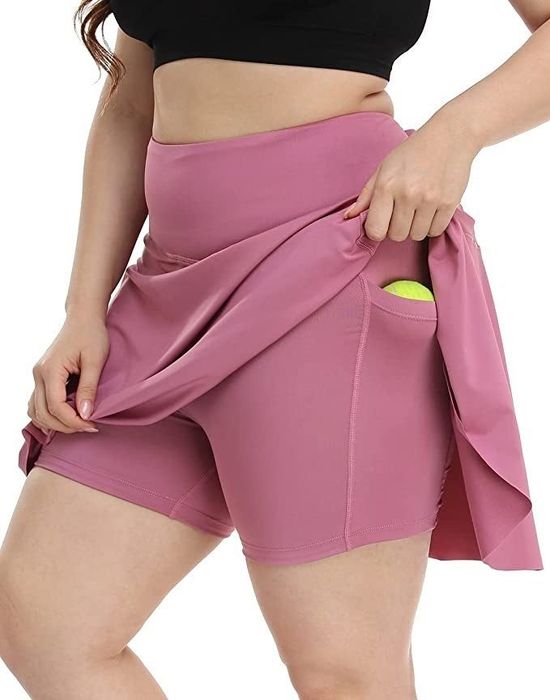 A model wearing a pink skirt, highlighting the shorts underneath and a tennis ball tucked into the pocket.