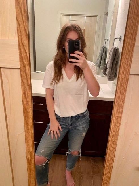 A mirror selfie of a reviewer showcasing the white V-neck tee paired with stylish ripped jeans.