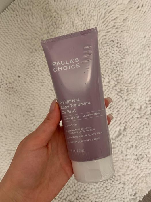 A hand holds a tube of Paula’s Choice body exfoliator cream.