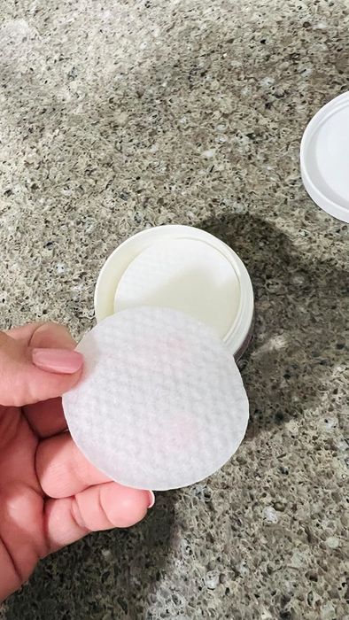 The same reviewer’s image of them holding one of the First Aid Beauty ingrown hair pads with the jar in the background