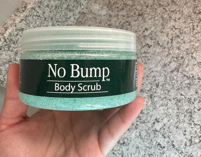 A photo showing a hand holding a jar of 'No Bump Body Scrub' against a marble countertop background.