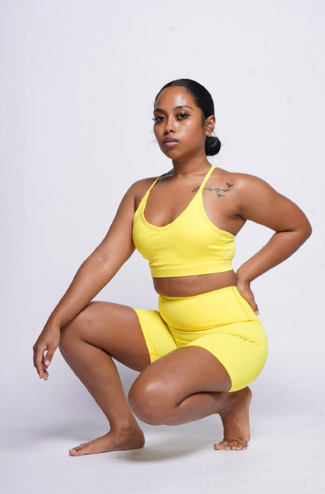 The model is wearing a yellow sports bra paired with matching bike shorts.
