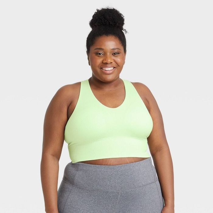 The model is wearing a light green, longline seamless sports bra paired with gray leggings.