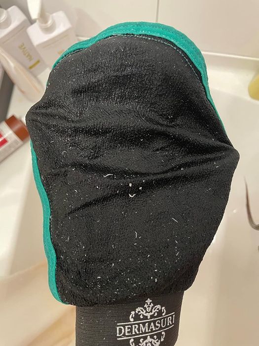 An exfoliating mitt rests on a bathroom counter, coated with skin particles from use.