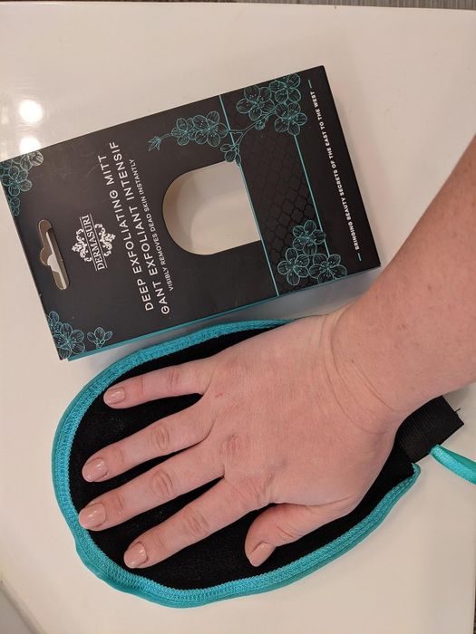 A reviewer is seen holding the exfoliating mitt in their hand.
