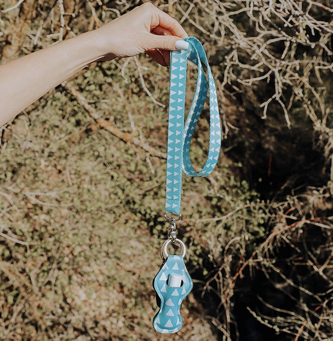 The model is holding the lip balm holder attached to a matching light blue lanyard.