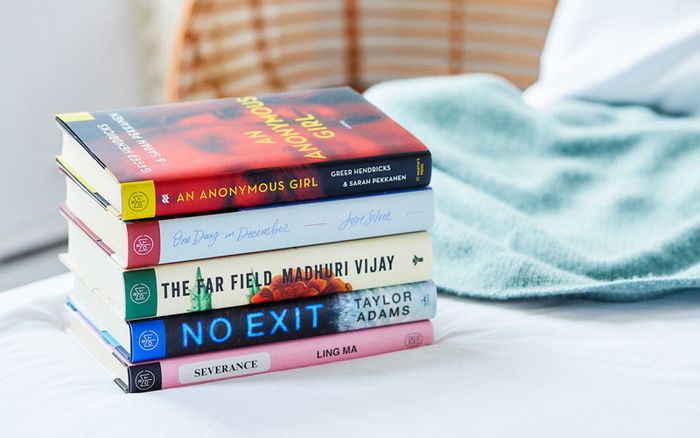 A stack of five books neatly arranged on a bed.