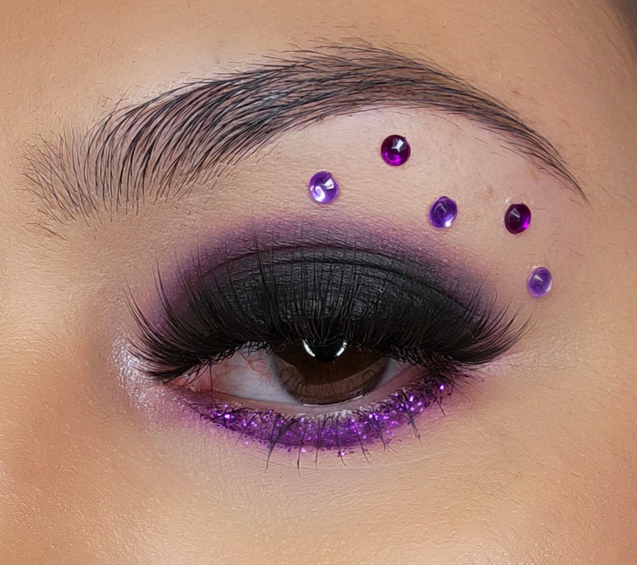 A reviewer adorning purple gems along their brow bone to complement their eyeshadow