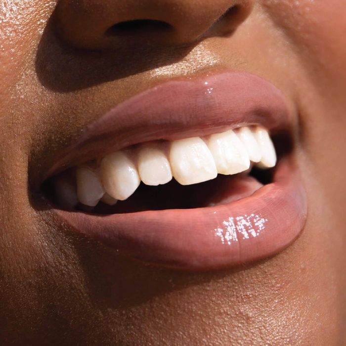 A model wears the gloss in a soft, milky pink hue.
