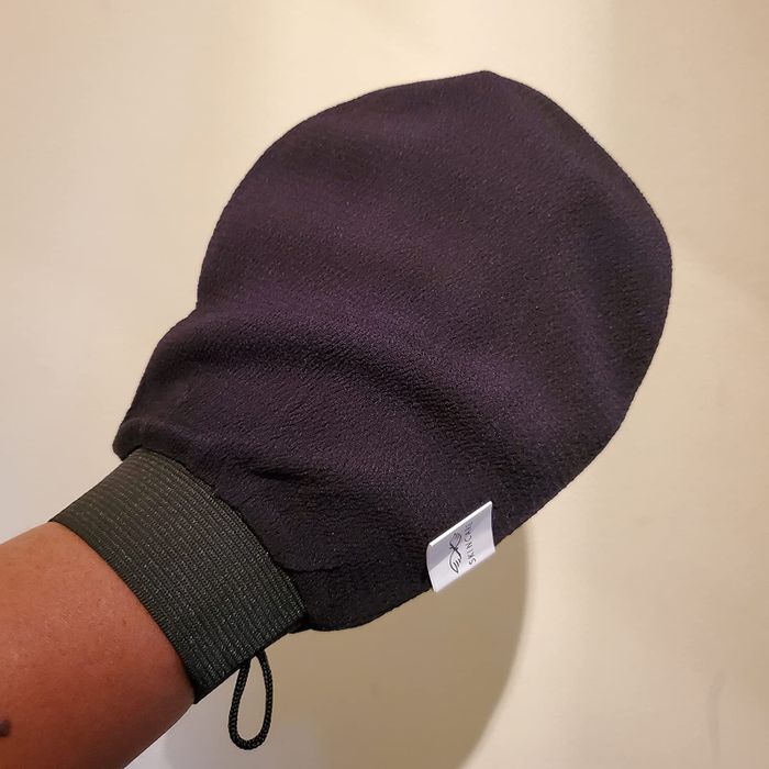 A reviewer holding the black exfoliating mitt in their hand