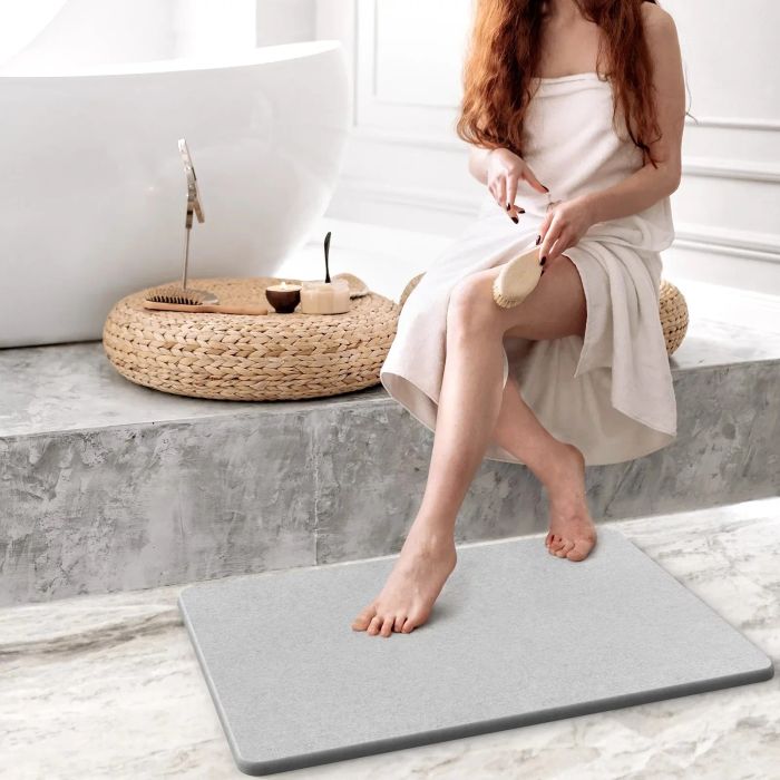 A model seated on a step beside a bathtub, stepping onto a stone bath mat.