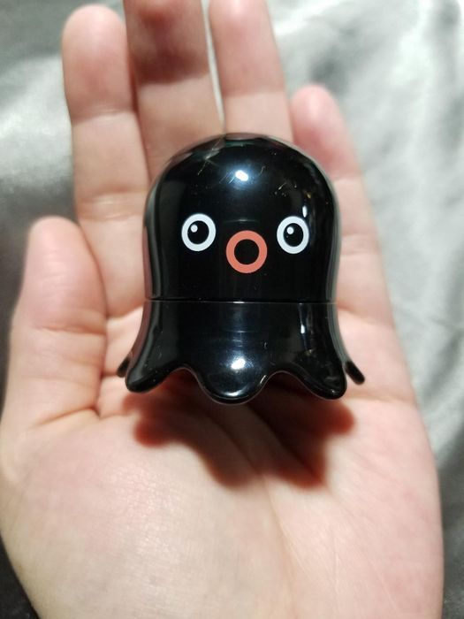 A person gently holding a small black figurine with cartoon-like eyes and a simplistic face in the palm of their hand