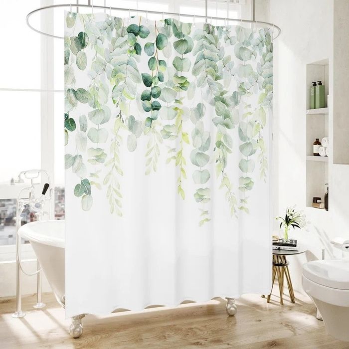 A shower curtain featuring a botanical print of cascading green eucalyptus leaves in a modern bathroom with minimalistic design, wooden flooring, and white fixtures.