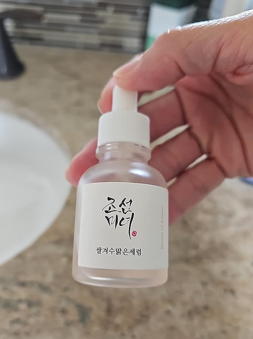 A reviewer holding a bottle of the Beauty of Joseon serum.