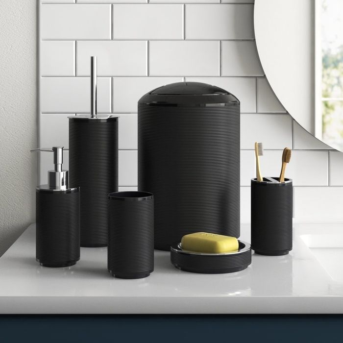 A modern black bathroom accessory set featuring a soap dispenser, toothbrush holder, and soap dish neatly arranged on a countertop with a sleek, ribbed design.