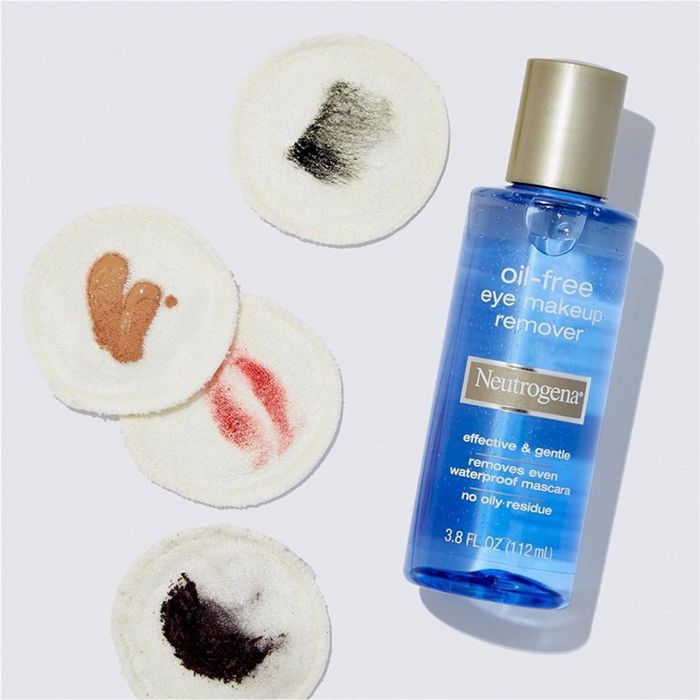 Neutrogena oil-free eye makeup remover bottle displayed beside four cotton pads with makeup stains in black, brown, and red.