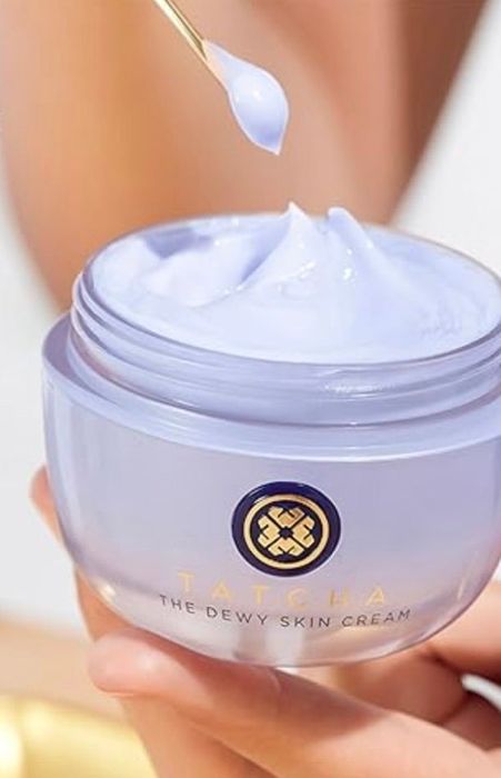 A close-up of a hand holding a jar of Tatcha Dewy Skin Cream, with a dropper dispensing the luxurious product.