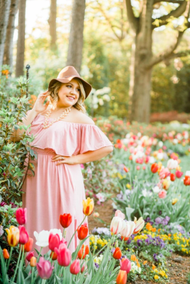 A reviewer wearing the dress, complemented by a hat and a bold necklace.