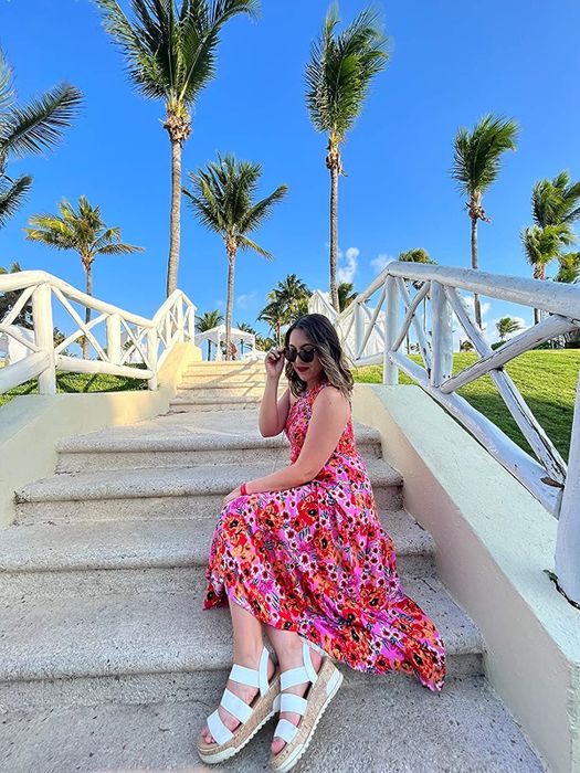 A reviewer wearing the dress in a vibrant mix of pink and orange, paired with white shoes.
