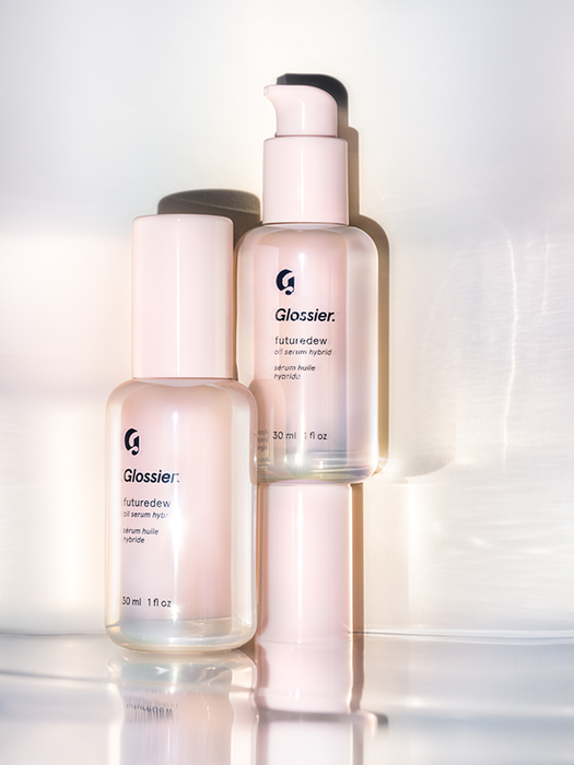 Bottles of Glossier's Futuredew hybrid serum, featuring pink and transparent designs