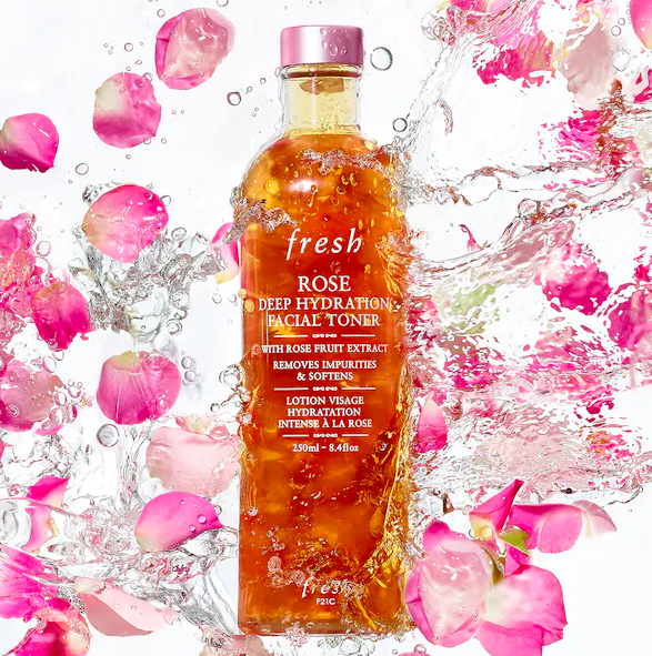 A bottle of Fresh Rose Deep Hydration Facial Toner, showcasing rose petals and a clear formula, set against a backdrop of pink roses