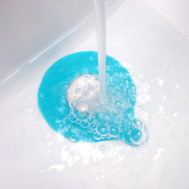 A blue tub stopper positioned beneath a running water faucet