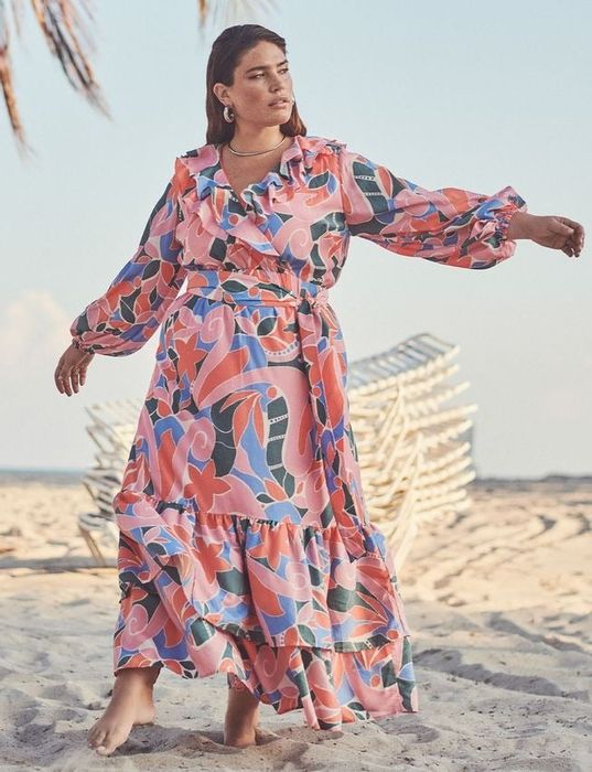 A model is wearing a beautiful floral dress while walking along the beach.
