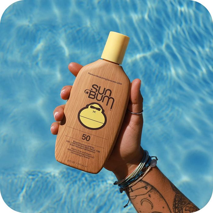 a hand holding a brown bottle of Sun Bum SPF 50 sunscreen