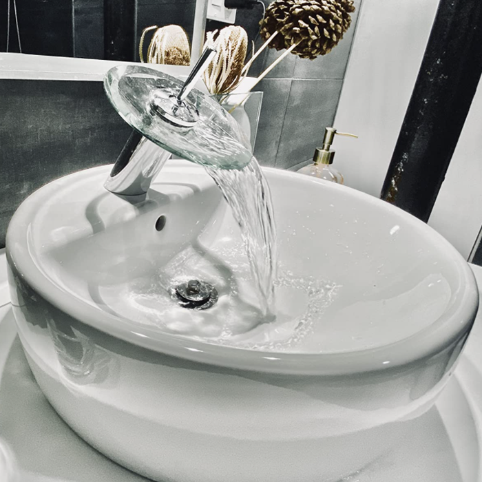 A close-up of the reviewer's raised bowl bathroom sink, featuring a faucet that dispenses water from the top, cascading off a clear dish for a visually striking effect.