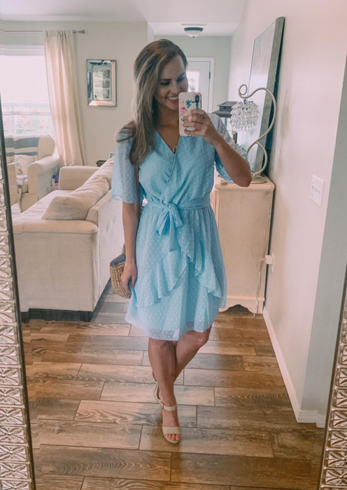 A reviewer wearing a light blue dress that falls above the knee