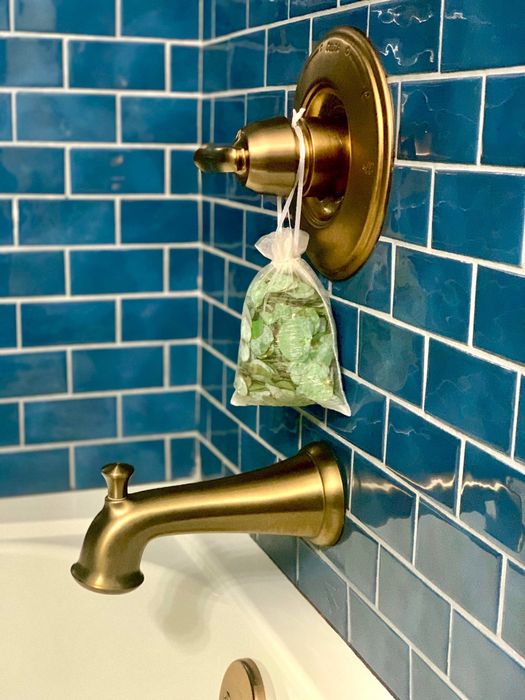 A eucalyptus shower pouch hangs from the handle valve of a bathtub.